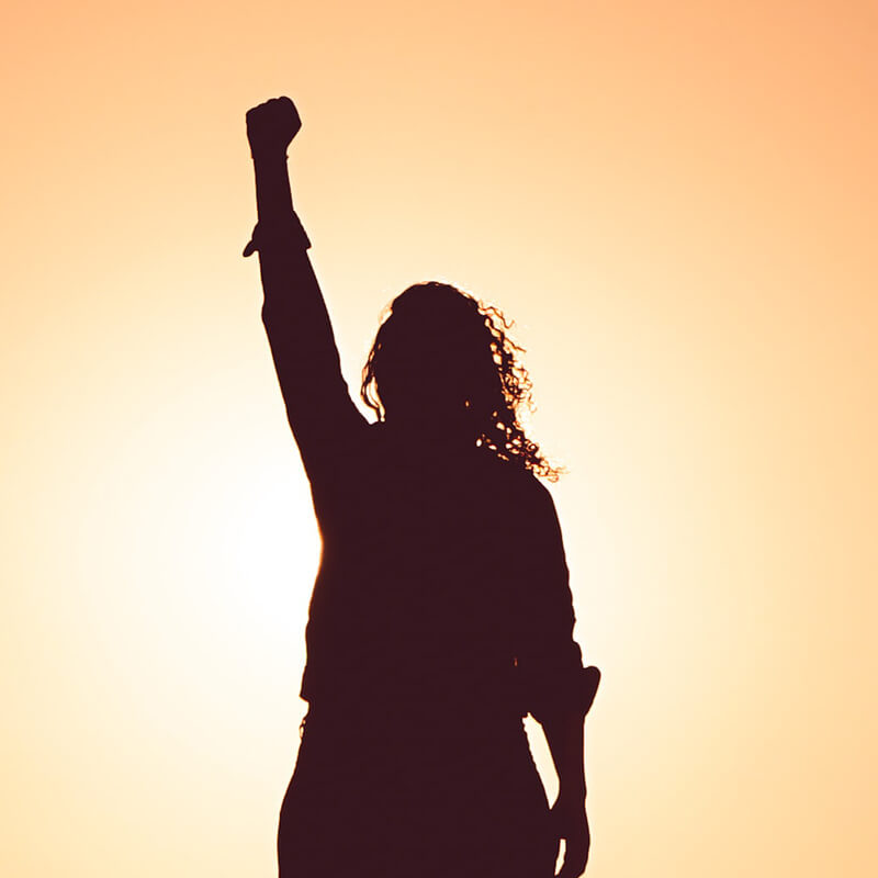 woman raising fist in front of sunset